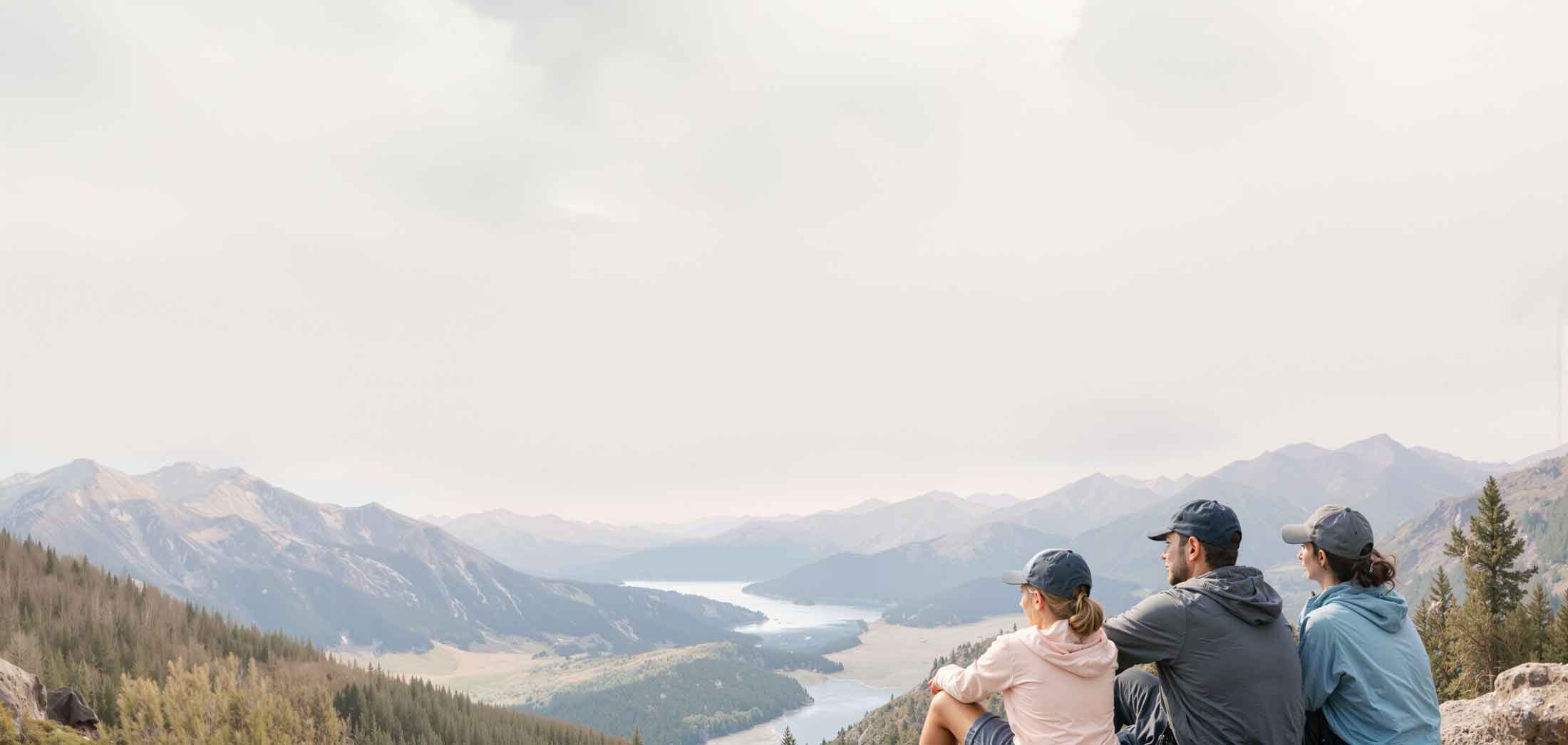 A family wearing our sun hoodies sitting on a rock, looking out at a scenic mountain landscape with a river.