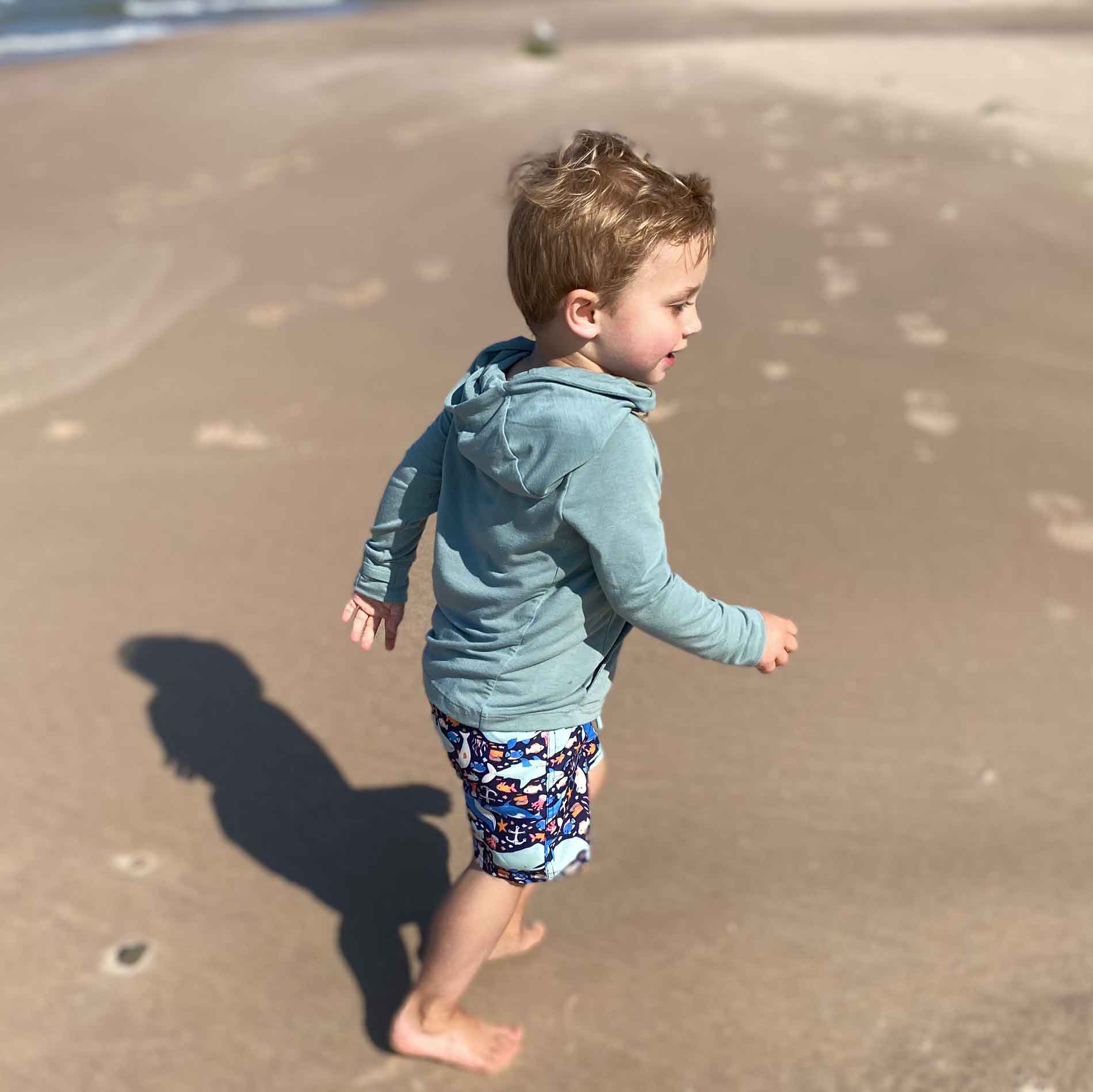 Toddler wearing CHASER sun hoodie with UPF 50+ running on beach for sun protection.