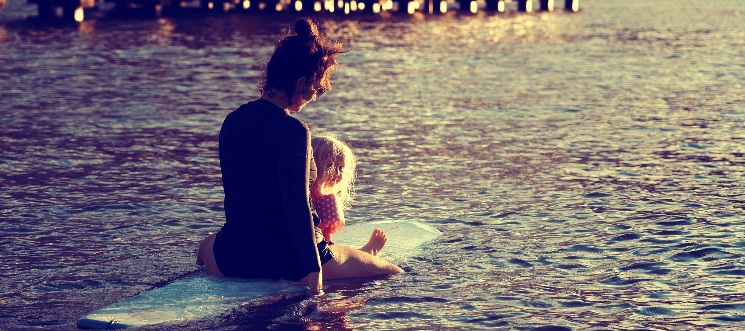 Milk x Whiskey - A mother and her daughter on a surfboard while on an adventure with the family. Sunset.