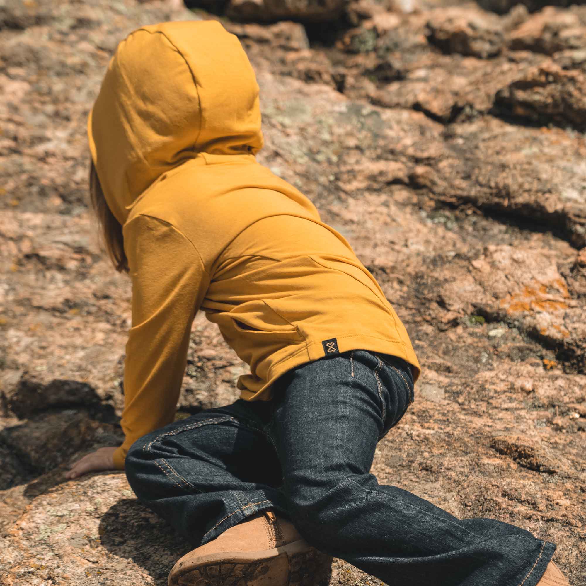 Toddler wearing yellow sun hoodie with UPF 50+ climbing rocks outdoors, showcasing sun protection and comfort.