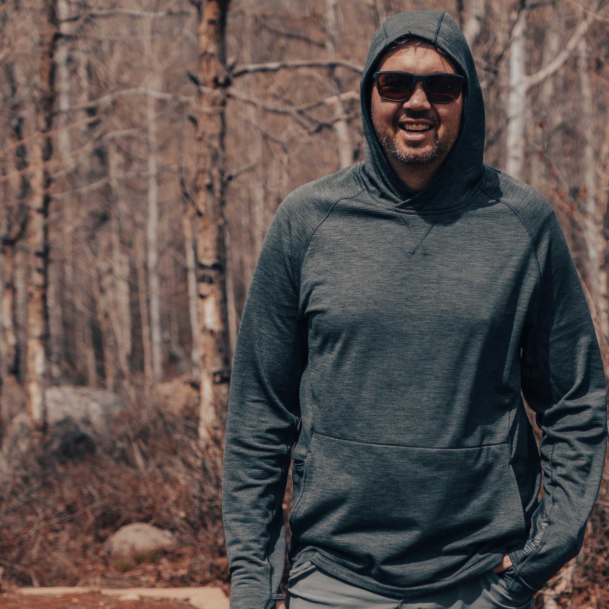 Man wearing Tumbler Grid Fleece Hoodie outdoors in forest setting, showcasing warmth and comfort during outdoor activities.